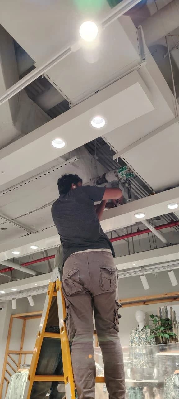 Technician on a ladder working on a ceiling AC unit