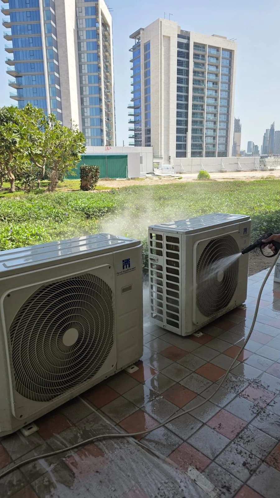 Outdoor AC units being washed on a rooftop with city towers behind