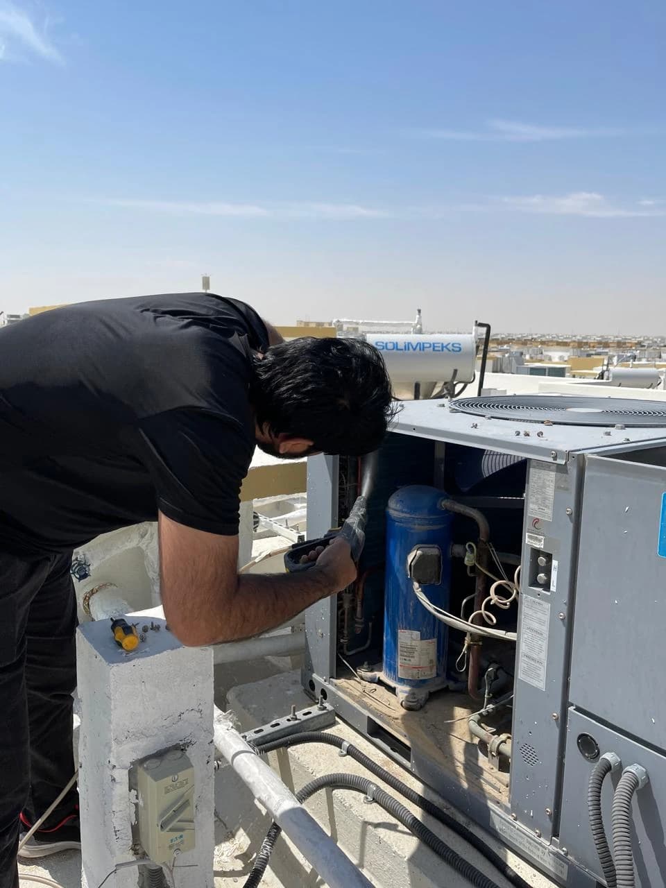Technician working on the compressor section of an open outdoor AC unit