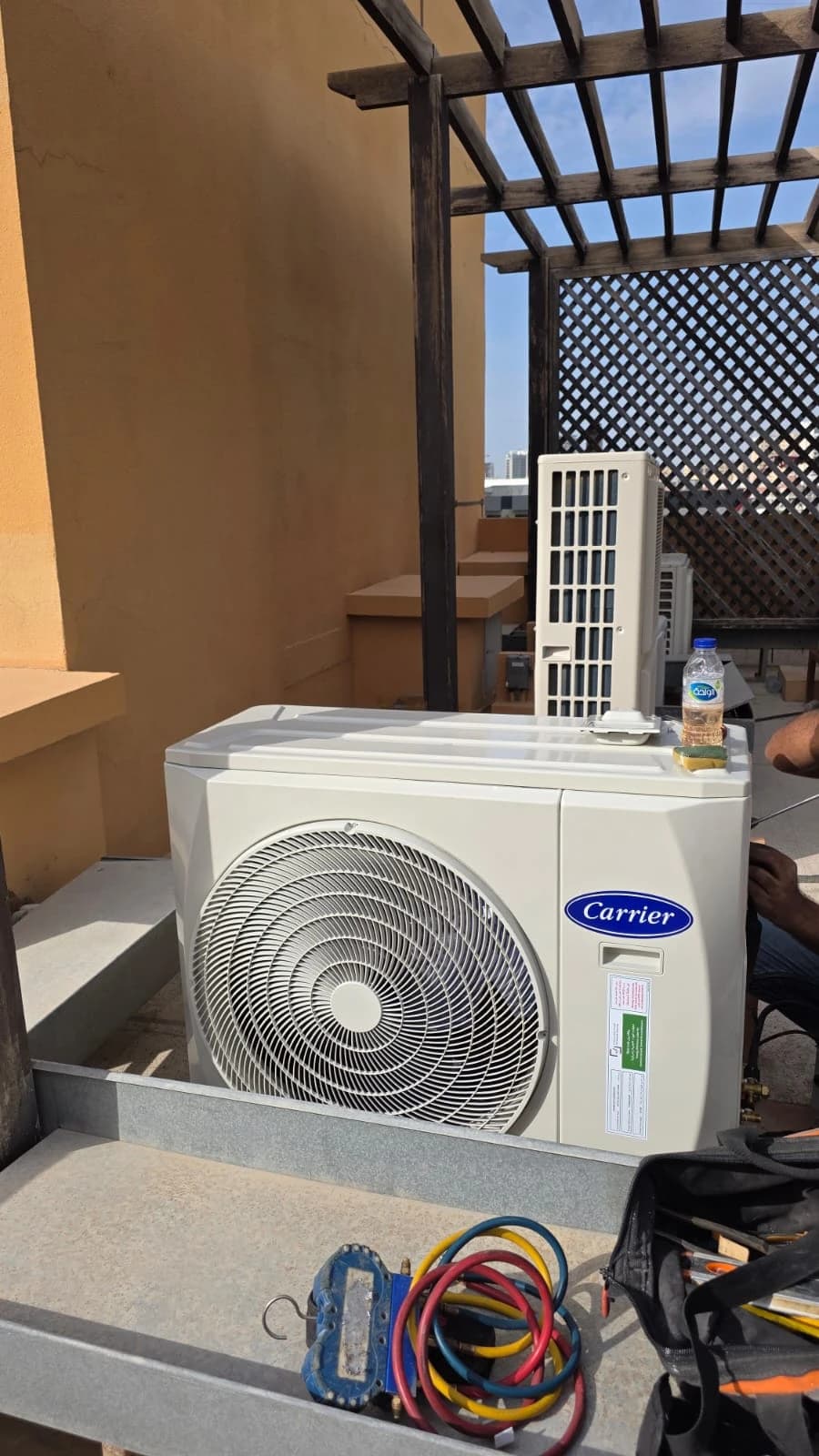 Outdoor split AC unit on a villa terrace with service tools and hoses