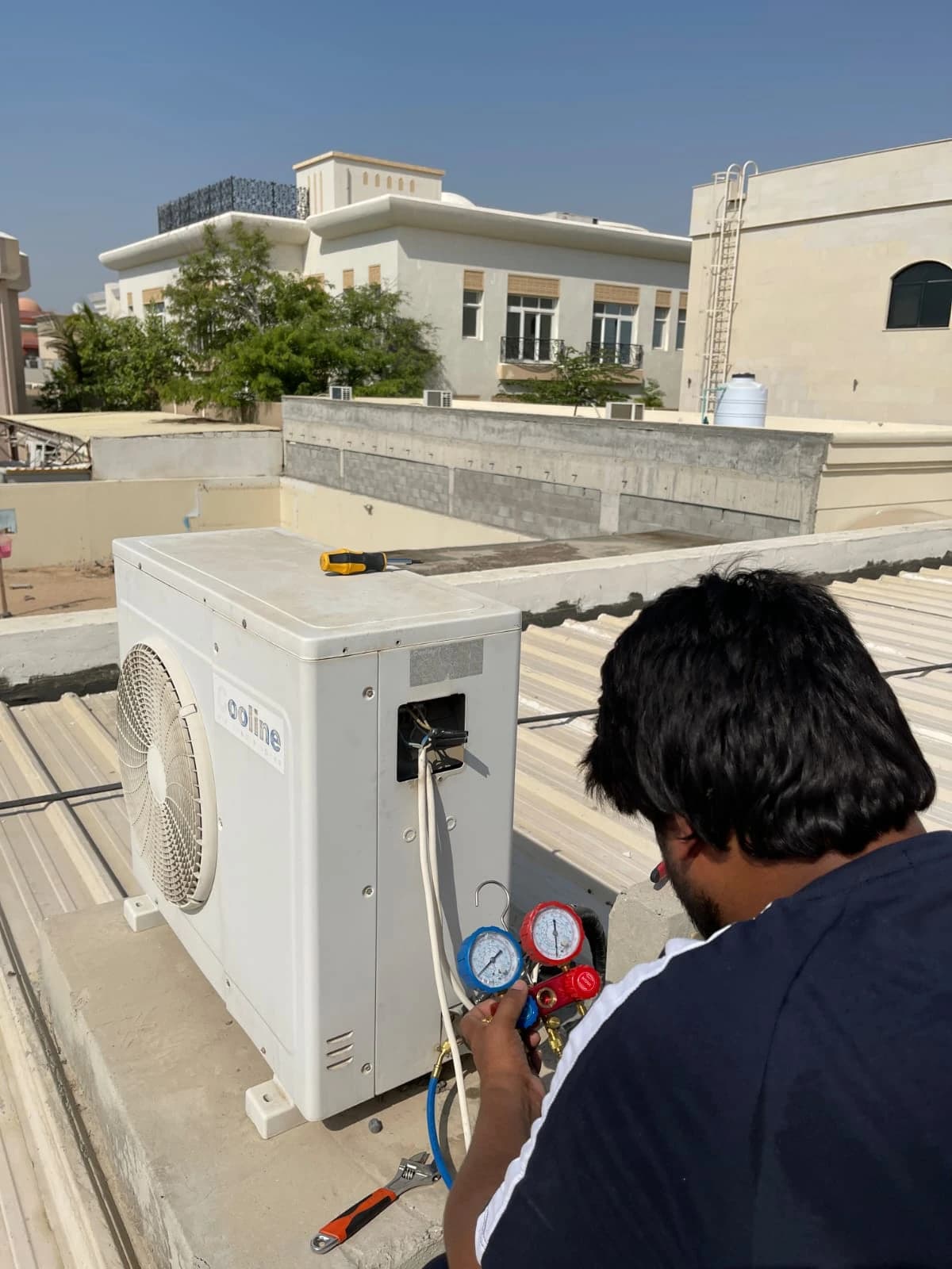 Technician checking an outdoor AC unit with pressure gauges on a rooftop