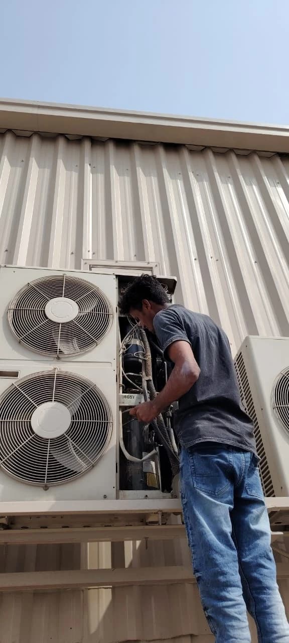 Technician servicing outdoor AC units mounted against a building wall