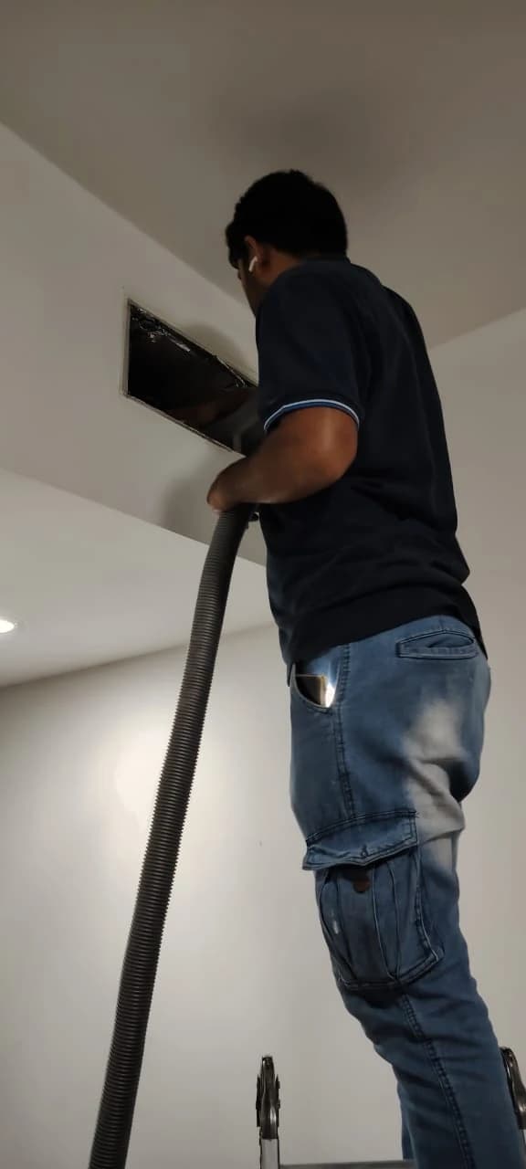 Technician vacuuming an AC vent on a ceiling