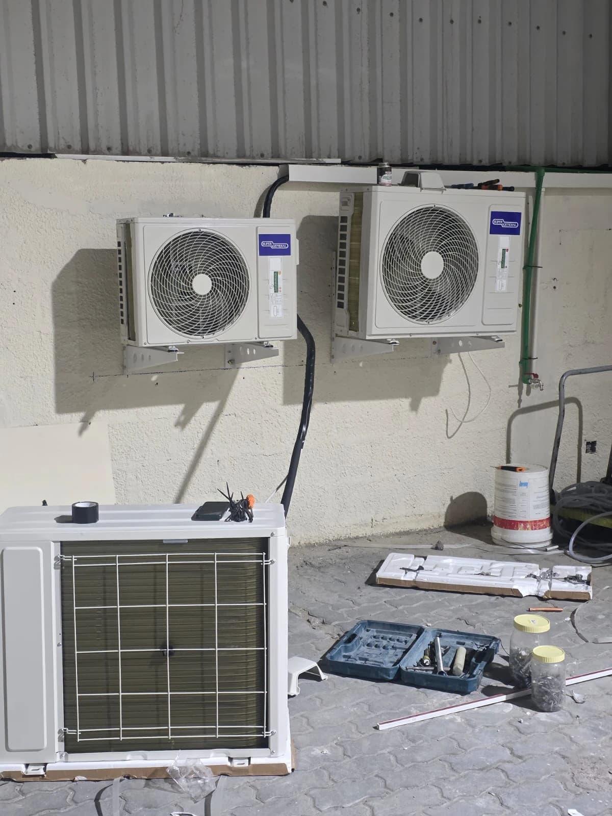 Outdoor AC units installed on a wall above a work area with tools
