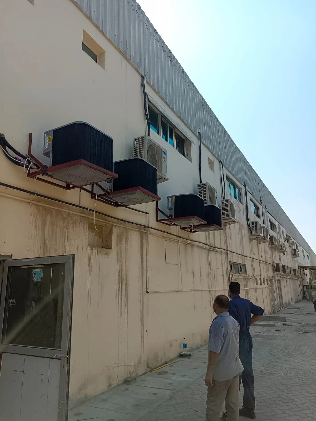 Technicians beside outdoor AC units along an industrial building wall