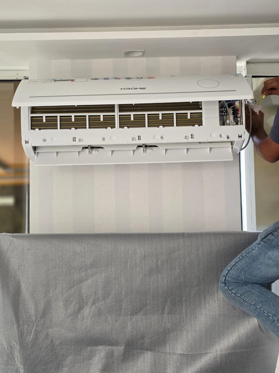 Wall-mounted split AC unit opened for cleaning with a protective cover underneath