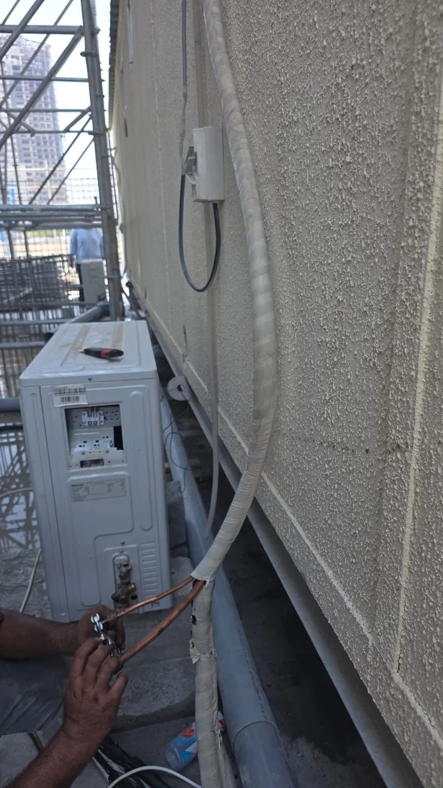 Refrigerant pipe connections being made at an outdoor AC unit on a building facade