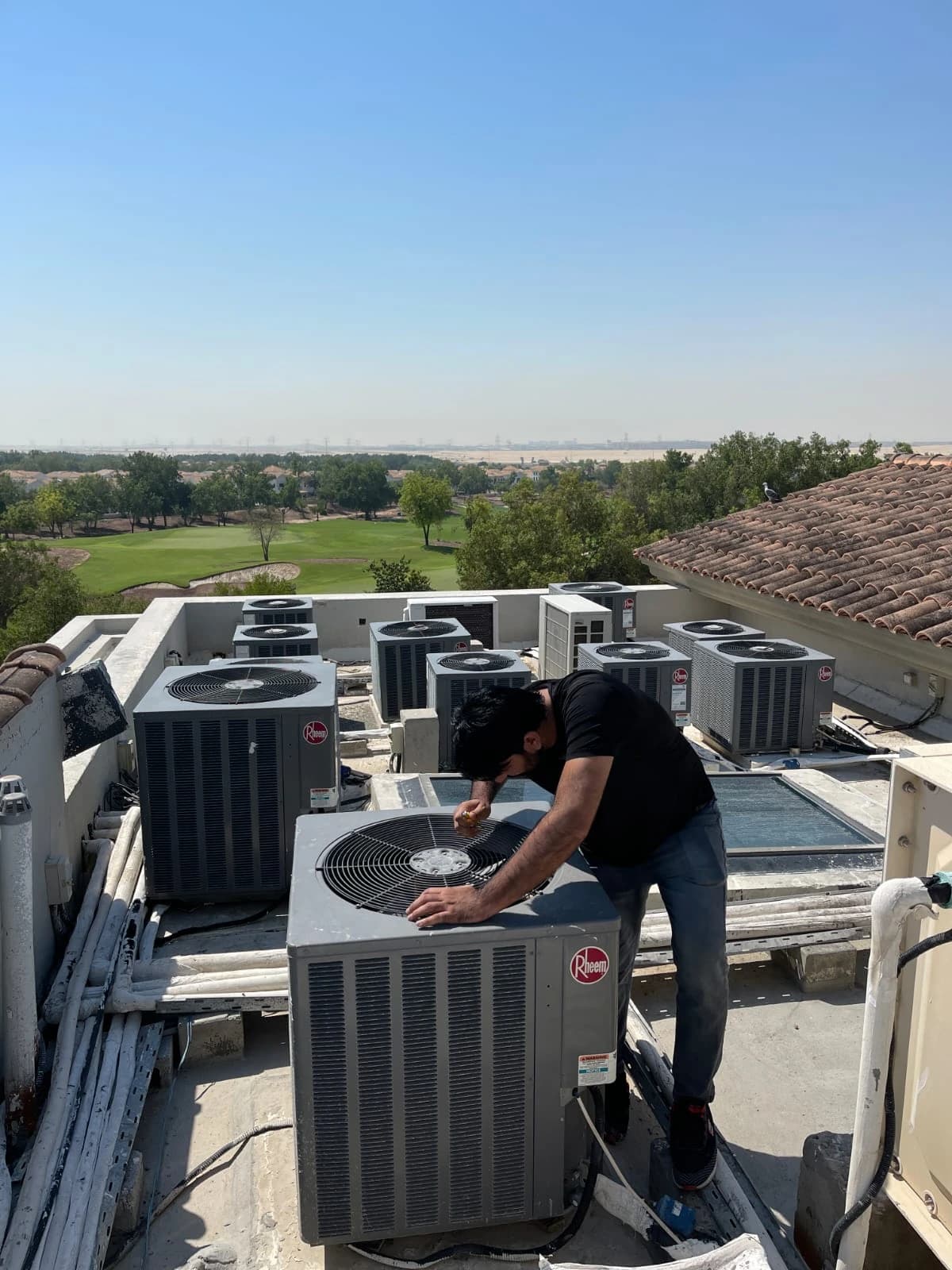 Technician maintaining a rooftop condenser unit with a golf course in the background