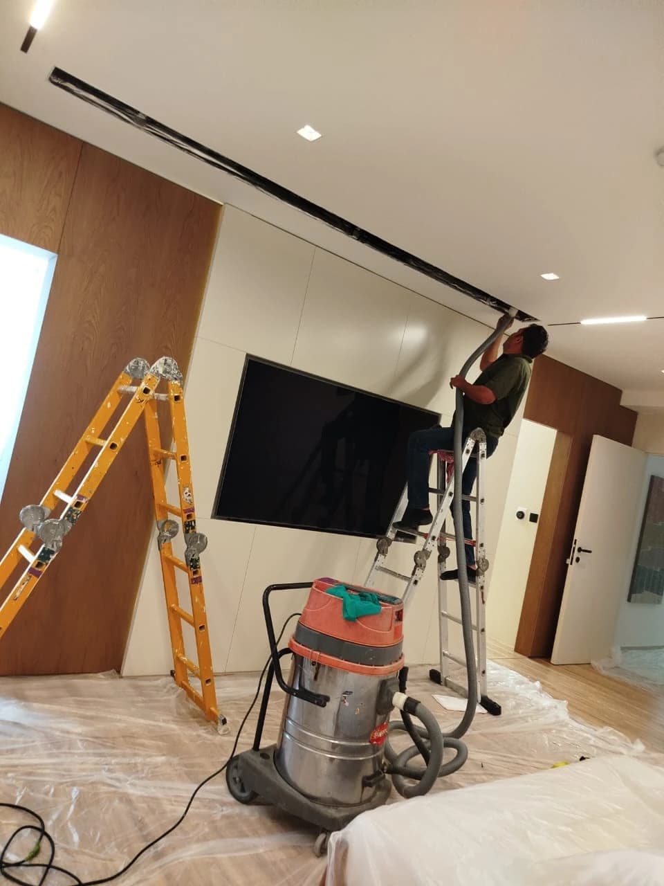Technician on a ladder at a ceiling vent with an industrial vacuum cleaner