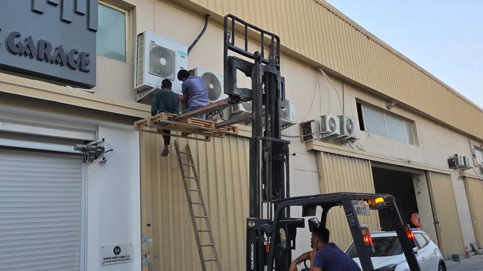 Technicians on a forklift platform installing an outdoor AC unit on a building